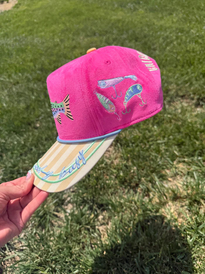 Pink cap with colorful designs held in front of a grassy background