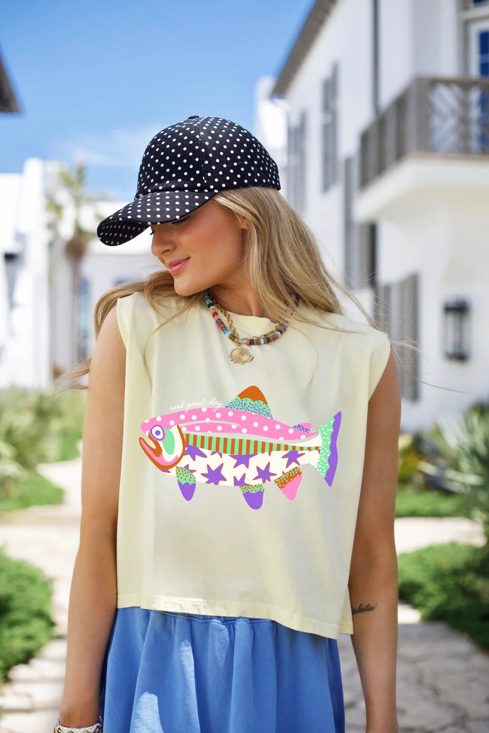 Woman wearing yellow tank with fish graphic standing outdoors