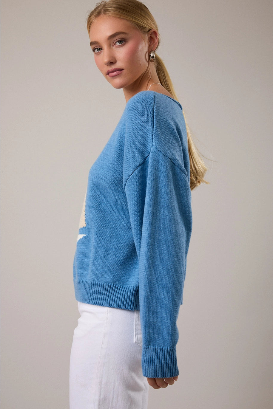 Woman wearing blue sweater and white pants on plain background