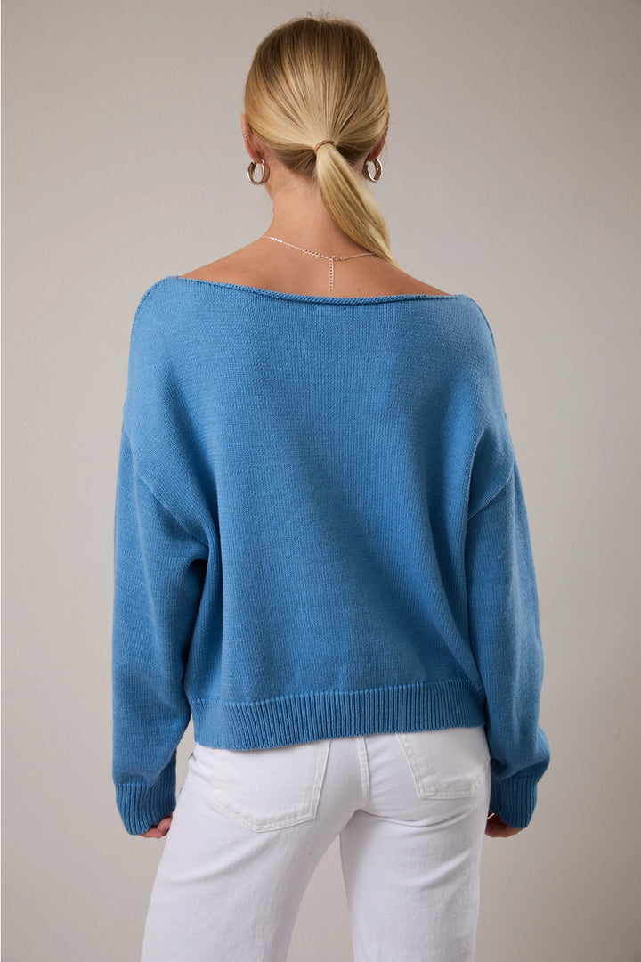Back of woman wearing blue sweater and white pants on plain background