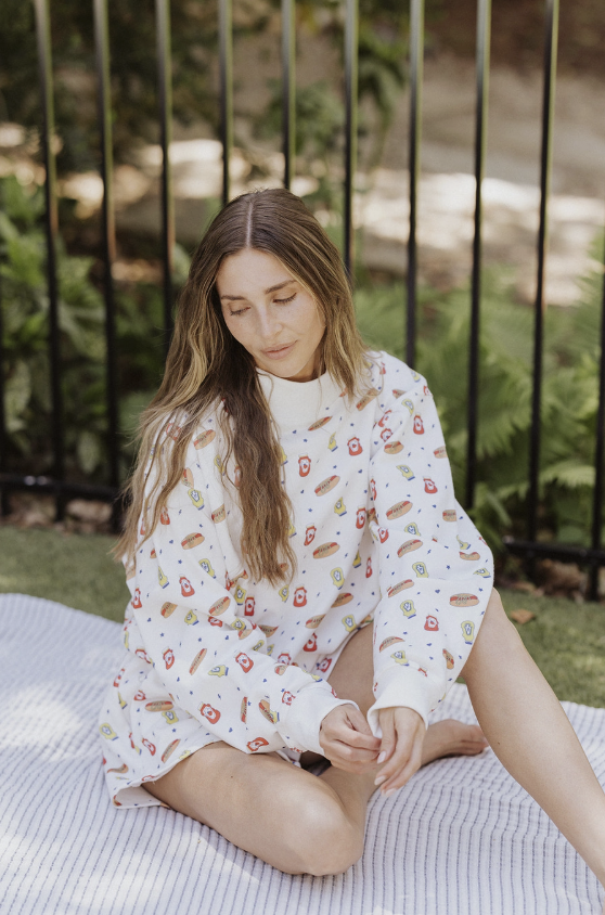 Woman sitting on a blanket outdoors wearing a white dress with a pattern.