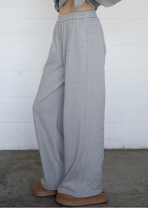 A person wearing loose, wide-leg striped pants and a cropped long-sleeve top, standing against a white painted brick wall on a concrete floor.