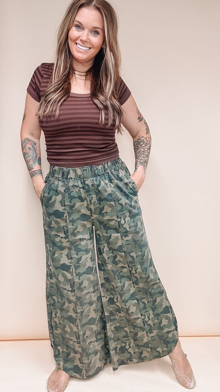 Woman wearing camo pants and brown stripe shirt on plain background