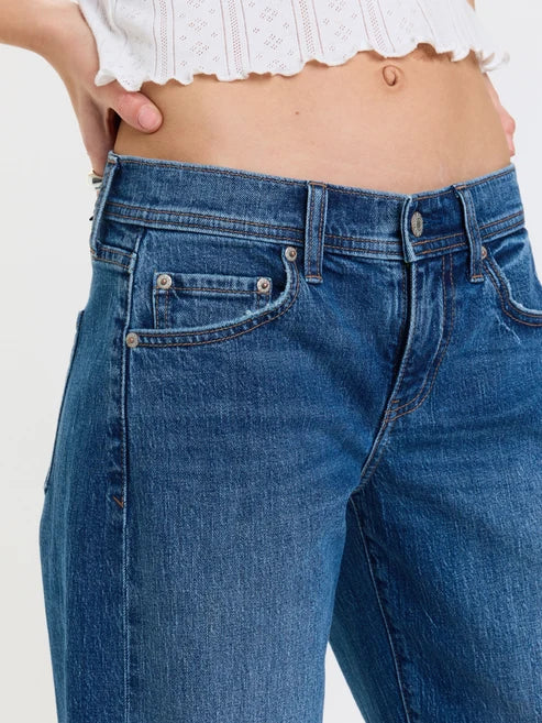 Close-up of a person wearing blue denim jeans with a white cropped lace top, showing the waist, hips, front pocket, and upper legs against a plain light background.
