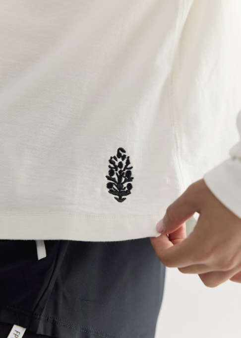 Close up detail shot of white long sleeve shirt with black logo on plain background