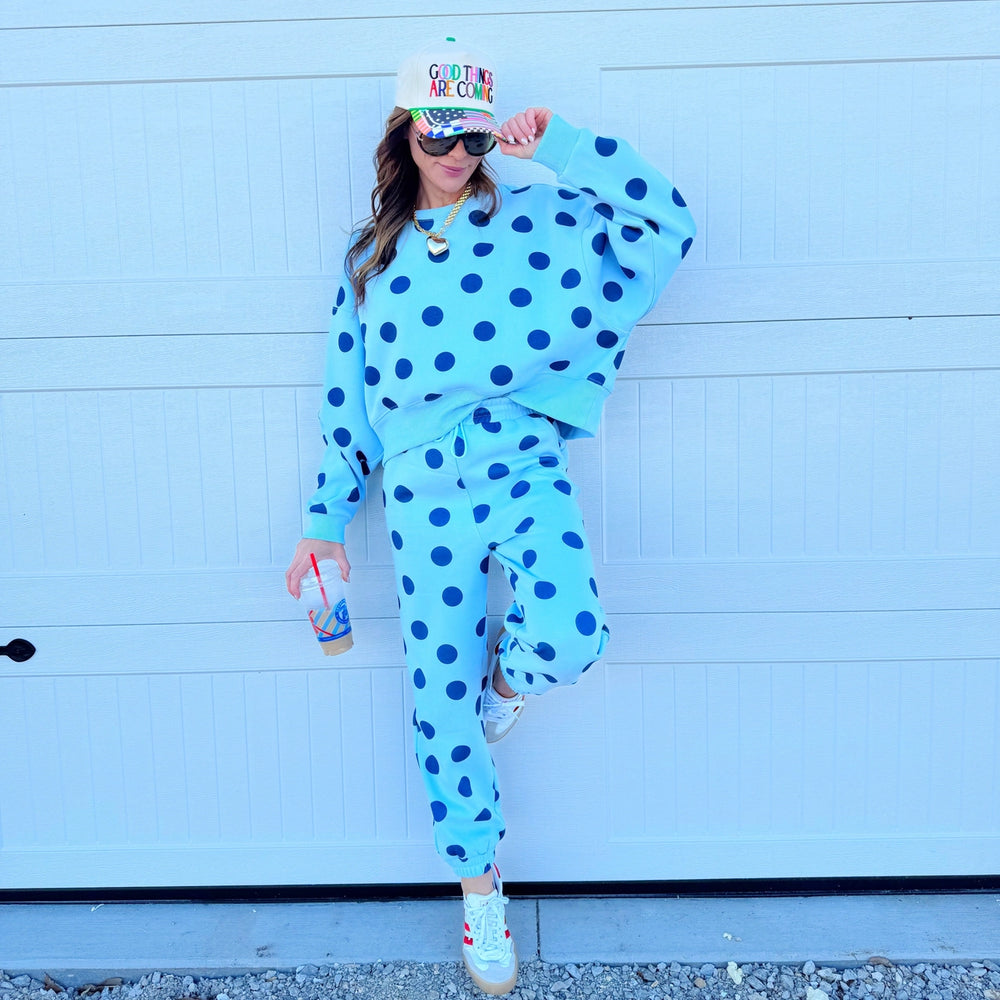 Person wearing a blue polka dot outfit with a colorful hat against a light blue wall.