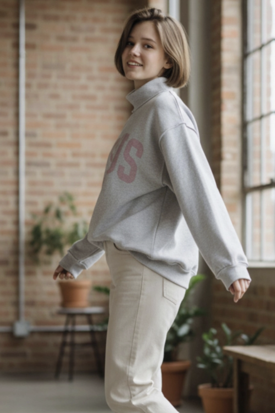 Woman wearing grey sweatshirt with pink writing and ecru denim standing inside house
