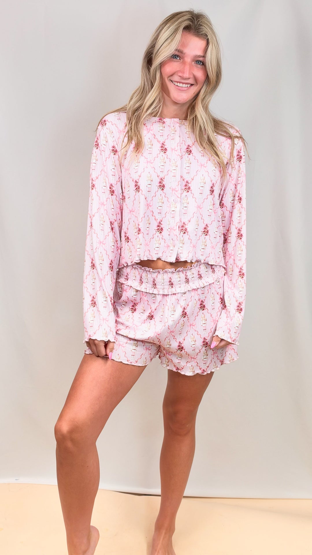 Woman wearing pink christmas pajamas with nutcrackers and bows on plain background