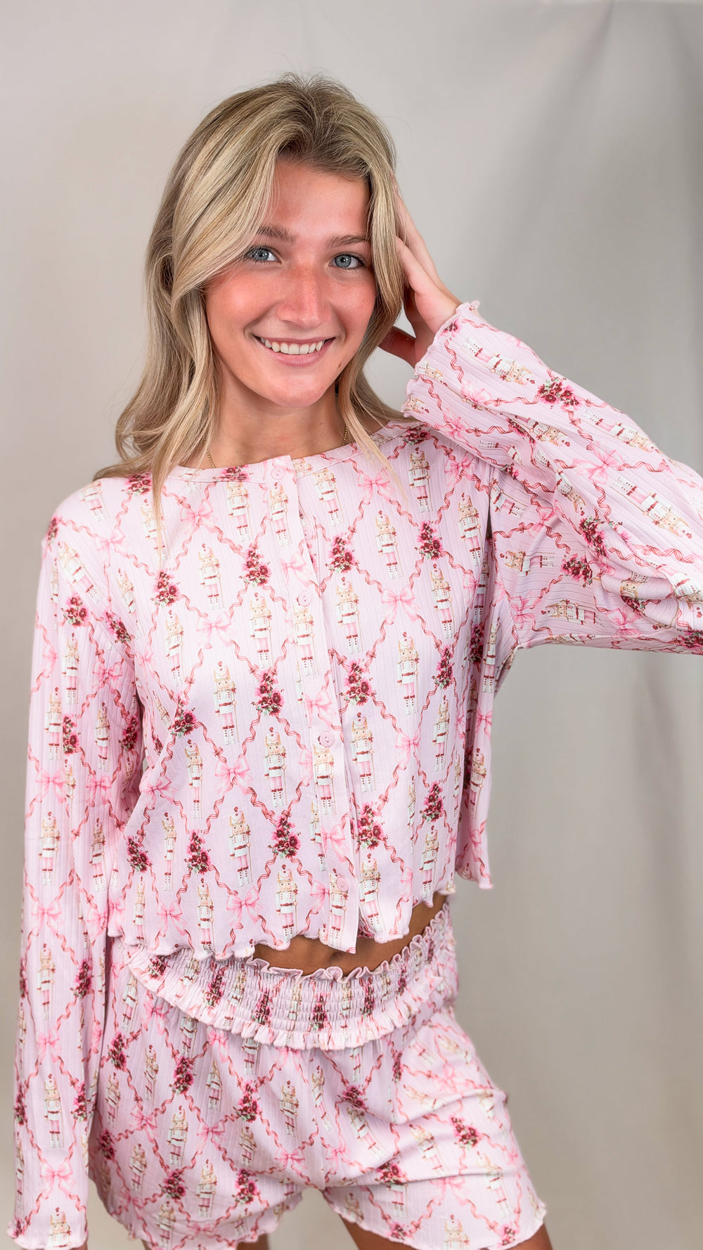 Woman wearing pink christmas pajamas with nutcrackers and bows on plain background