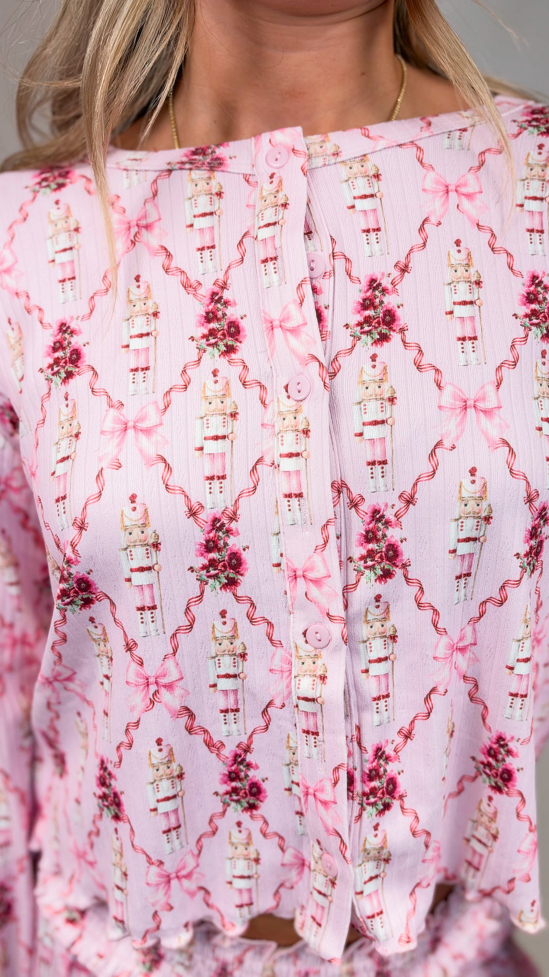 Close up of woman wearing pink chrismas pajamas with nutcrackers and bows on plain background