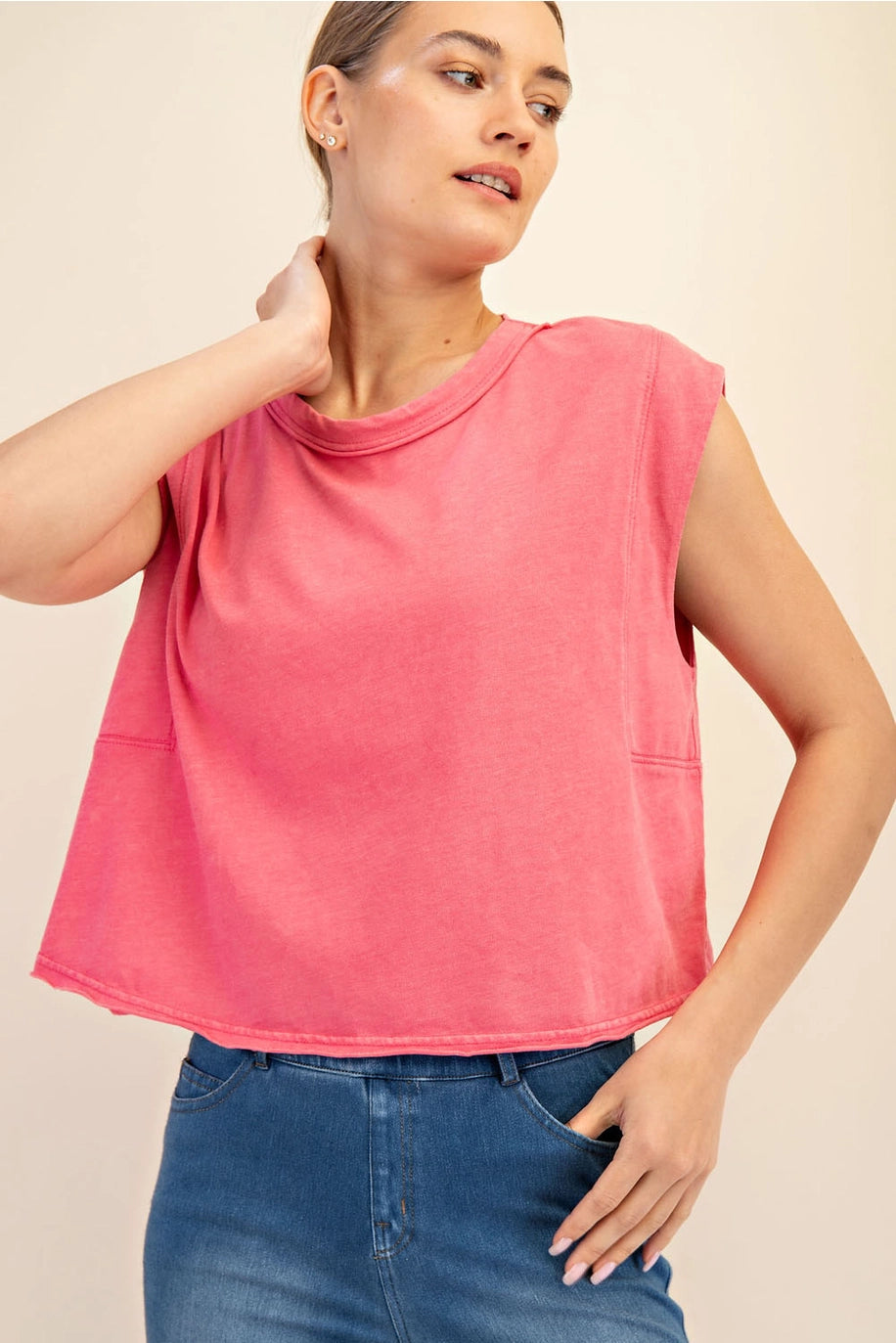 Woman wearing a pink sleeveless top and blue jeans on a beige background