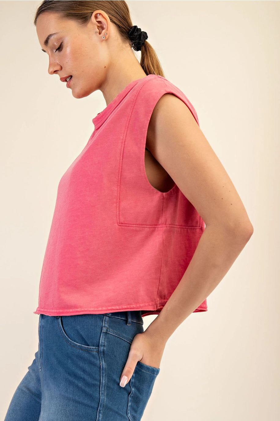 Woman wearing a pink sleeveless top and blue jeans against a beige background