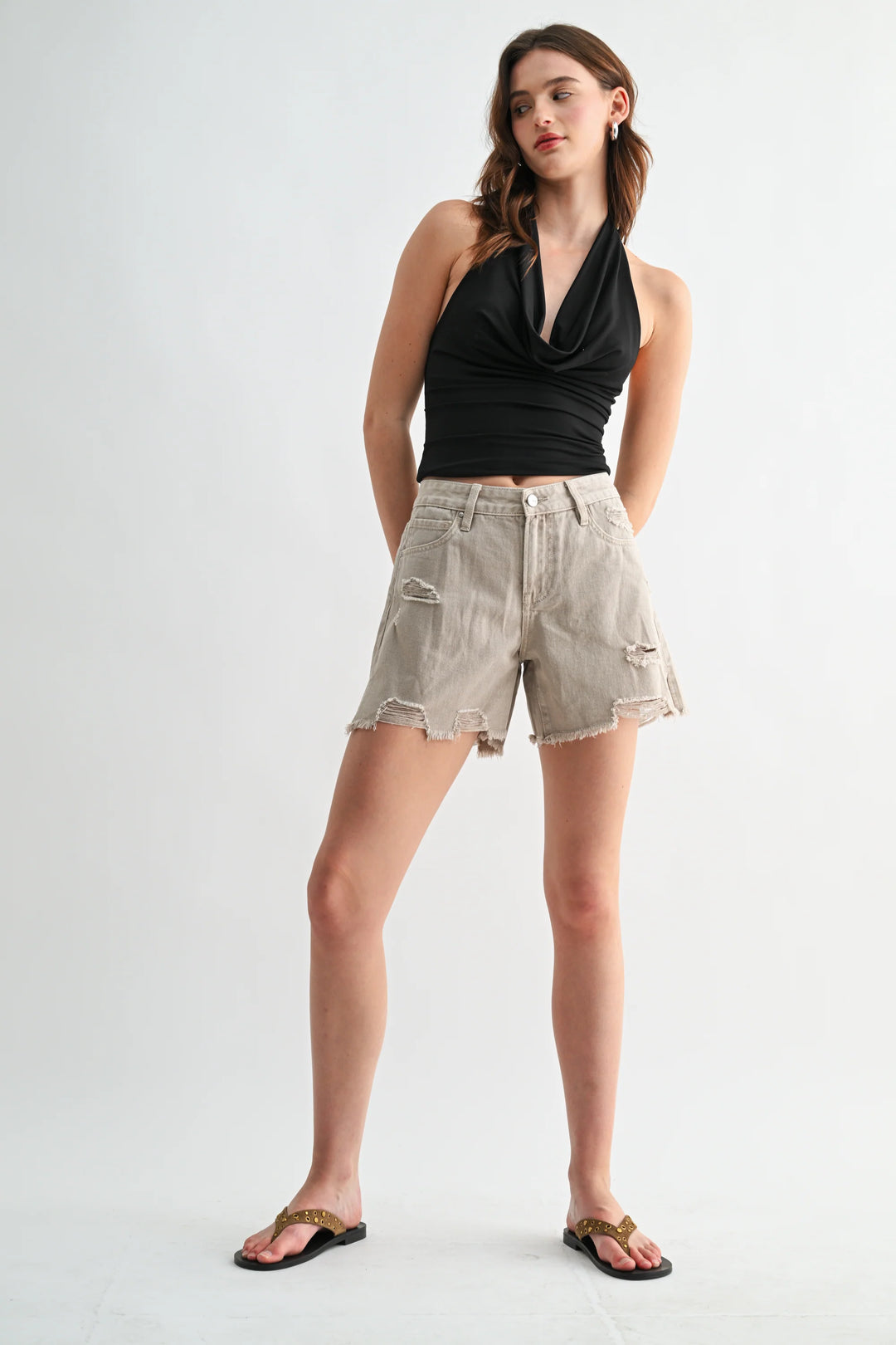 Woman wearing a black halter top and beige shorts on a white background