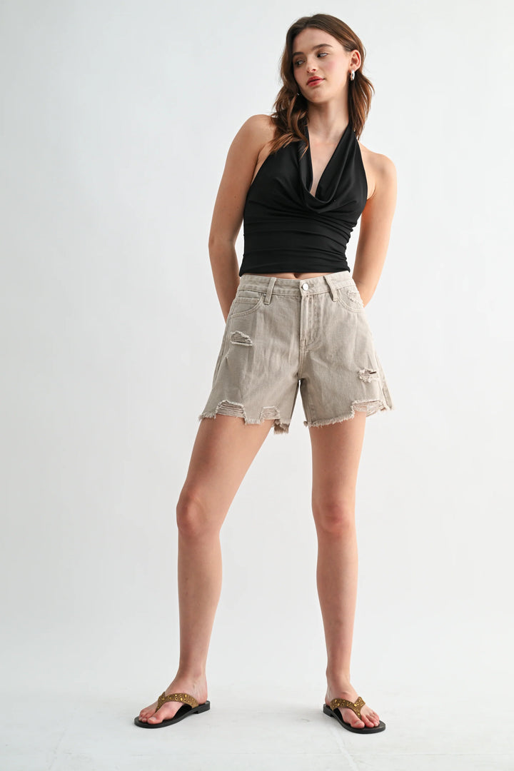 Woman wearing a black halter top and beige shorts on a white background