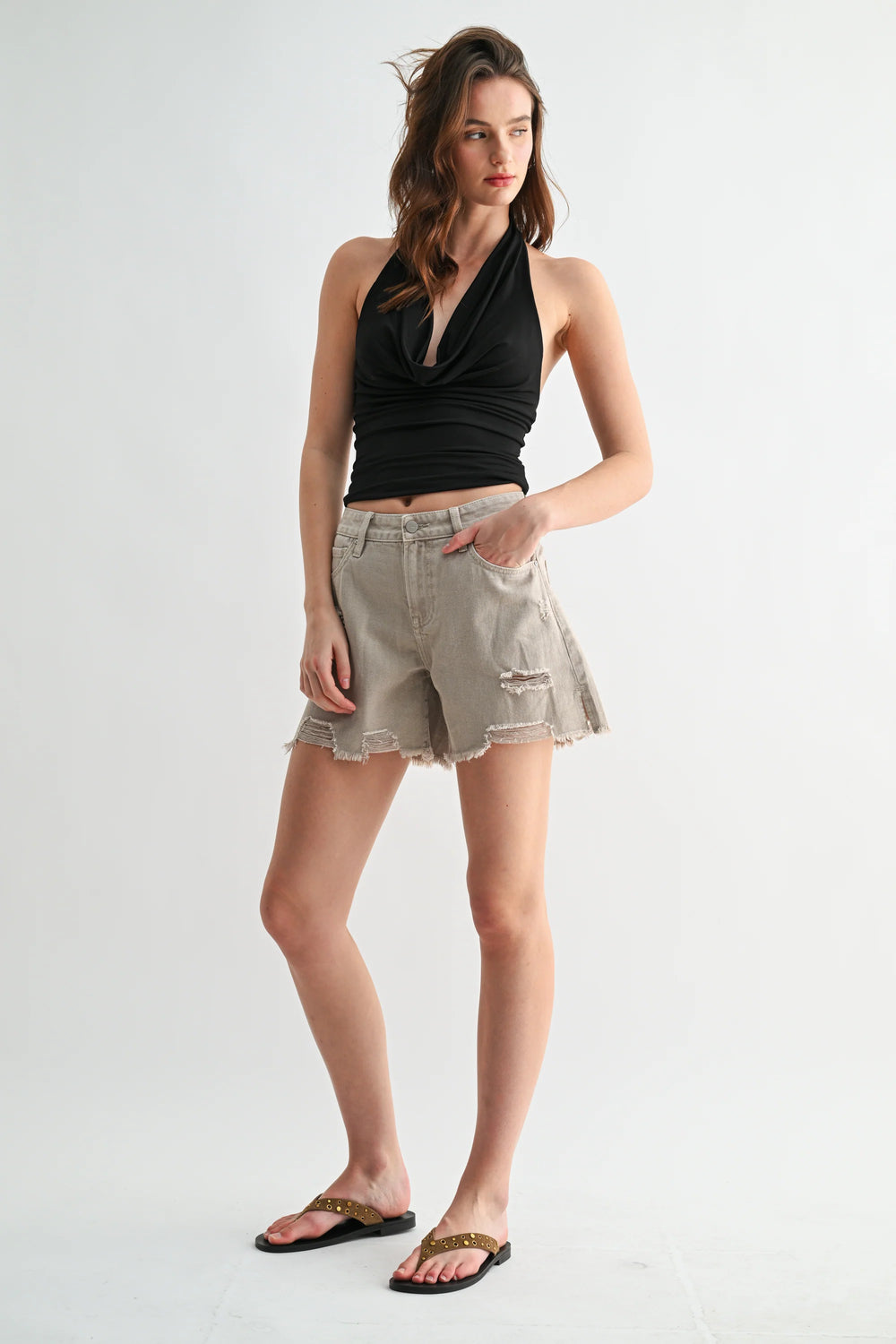 Woman wearing a black halter top and beige shorts on a white background