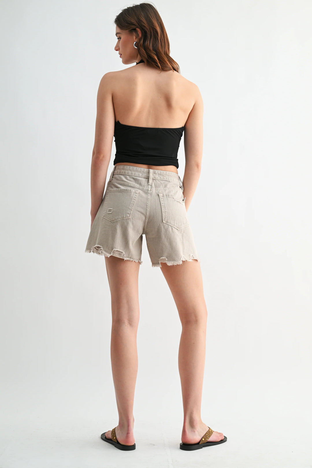 Woman wearing a black strapless top and beige shorts on a white background