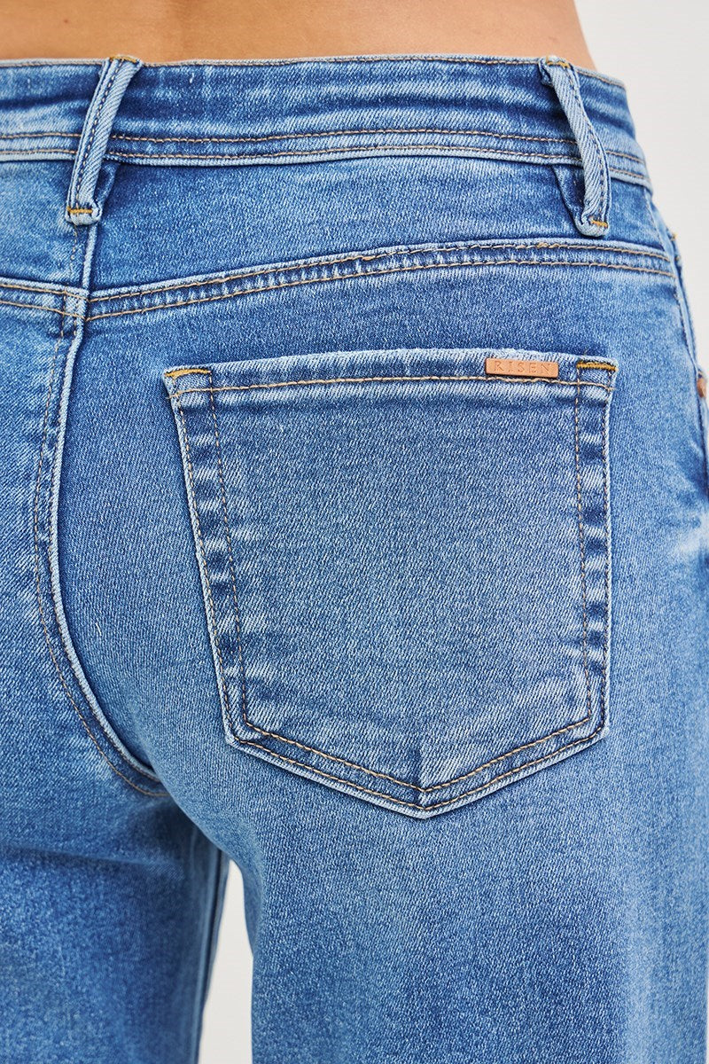 Close-up of the back pocket of blue denim jeans worn by a model, showing the fabric texture, stitching, and a small leather brand tab on the pocket.