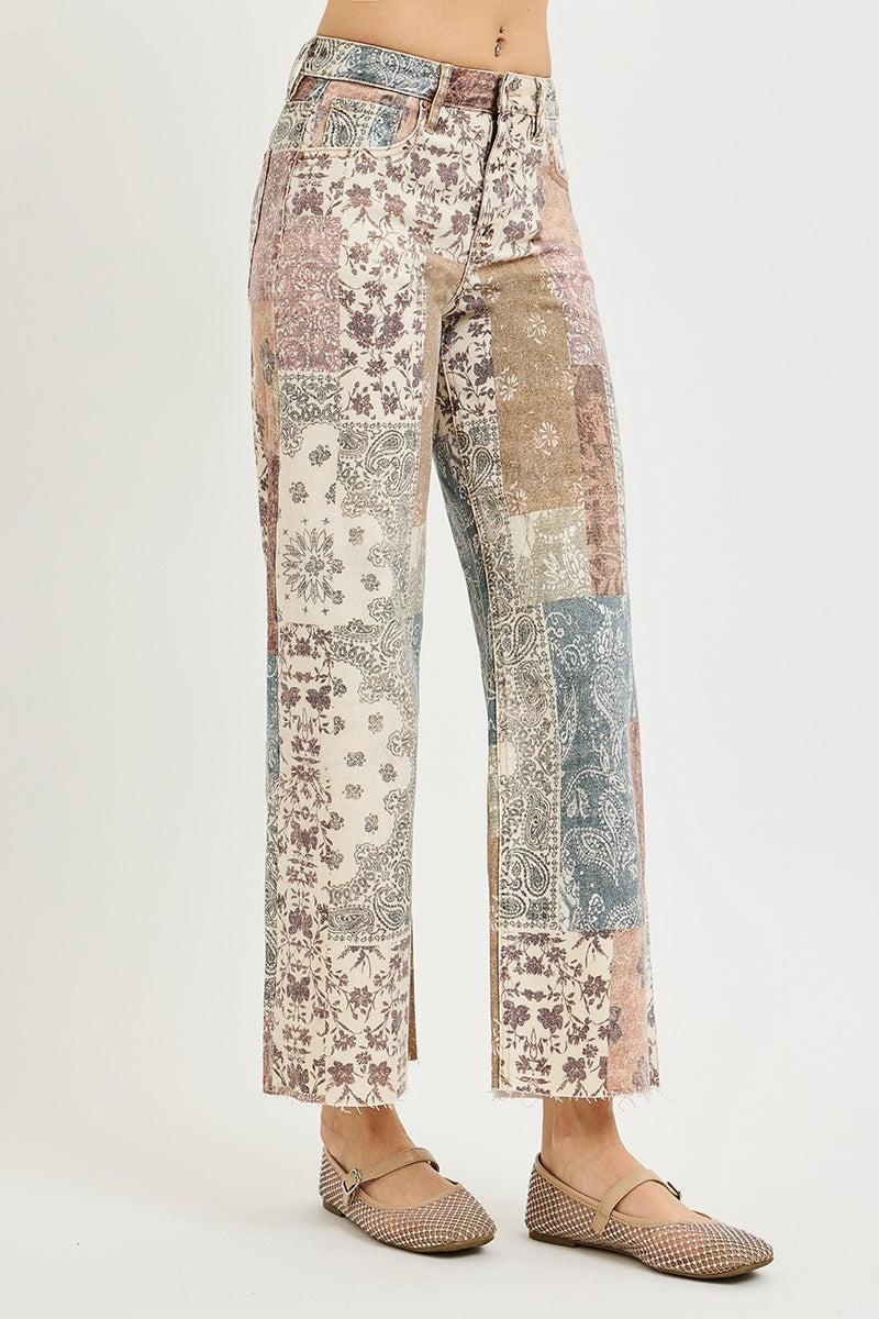 A model is shown from the waist down wearing a pair of wide-leg cropped pants with a multicolor patchwork print, paired with beige flat shoes, against a plain light gray background.