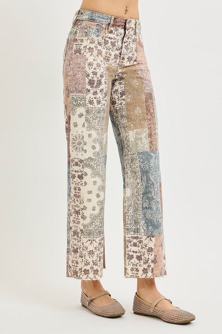 A model is shown from the waist down wearing a pair of wide-leg cropped pants with a multicolor patchwork print, paired with beige flat shoes, against a plain light gray background.