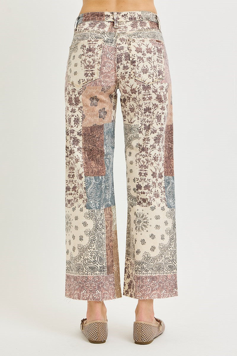 Patchwork wide-leg cropped pants with a distressed floral and paisley print in muted pink, beige, blue, and brown tones, shown on a model from the back against a light gray studio background.