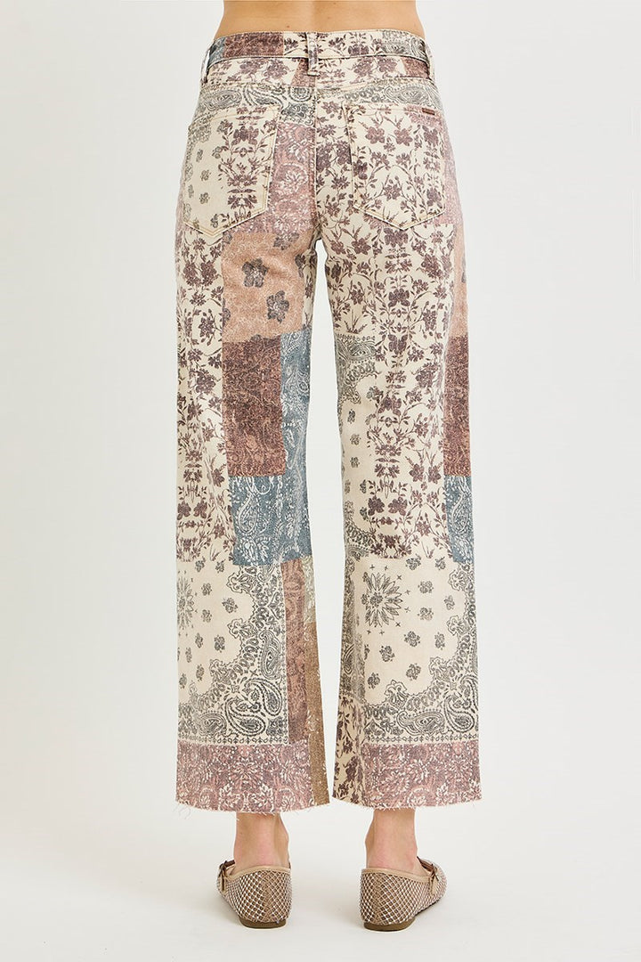 Patchwork wide-leg cropped pants with a distressed floral and paisley print in muted pink, beige, blue, and brown tones, shown on a model from the back against a light gray studio background.