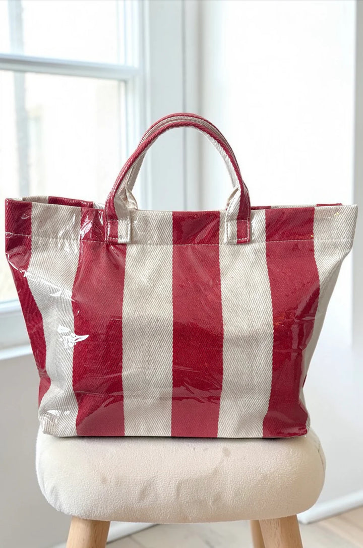 Red and white striped tote bag on a wooden stool with a white background