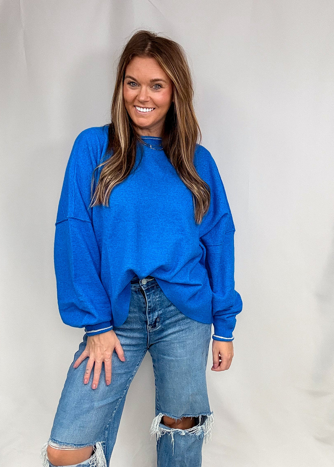 Woman wearing blue sweater with contrasting trim on neck and sleeves with jeans on plain background