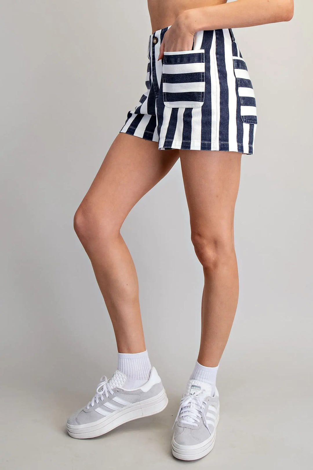 Person wearing navy and white striped shorts with white sneakers on a plain background