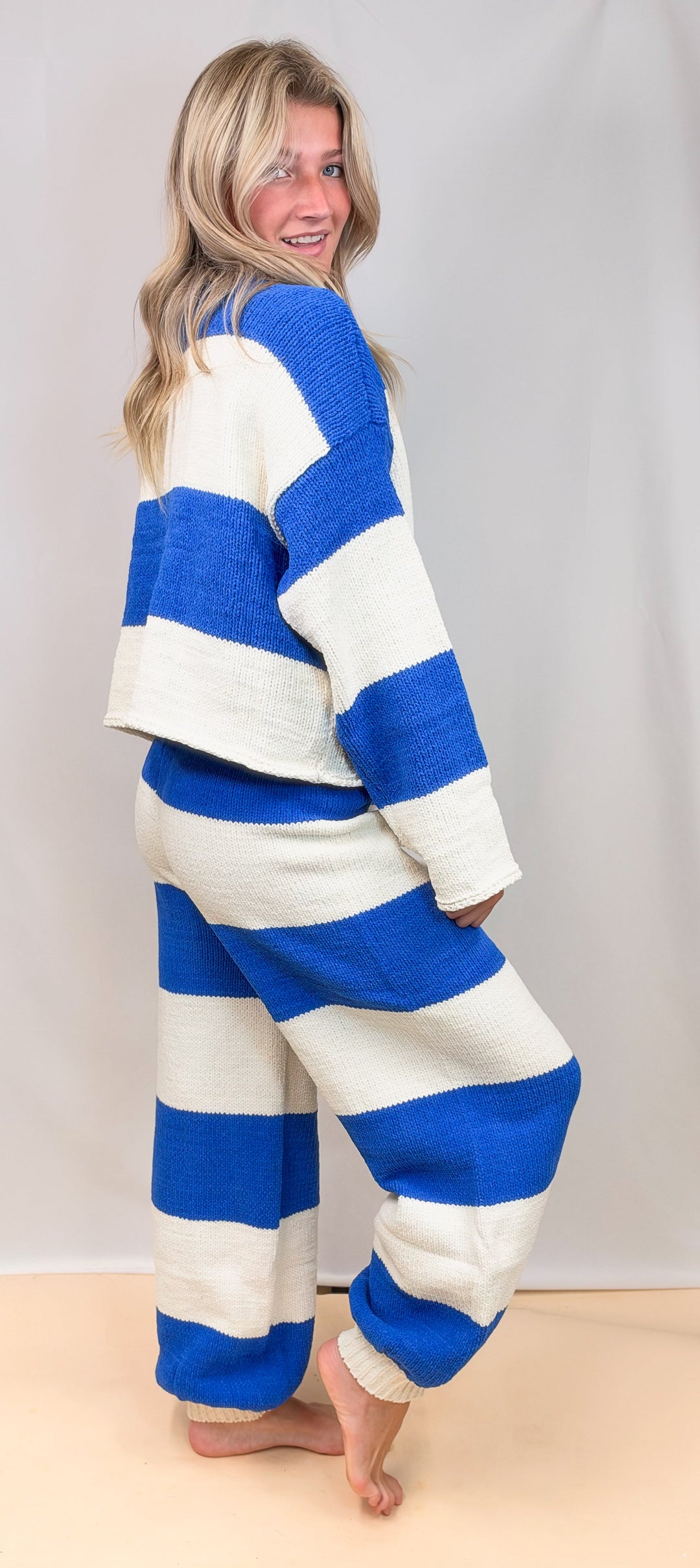A woman modeling a matching two-piece lounge set with bold blue and off-white horizontal stripes, photographed against a light neutral studio backdrop.
