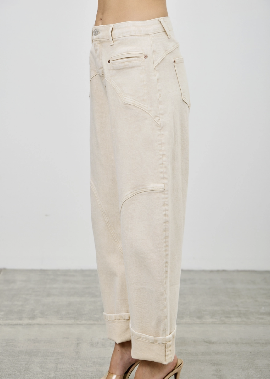 A person wearing off-white or cream-colored wide-leg cropped jeans with rolled cuffs and side pockets, paired with clear-strap high-heeled sandals, shown from the waist down against a plain light wall and gray floor.