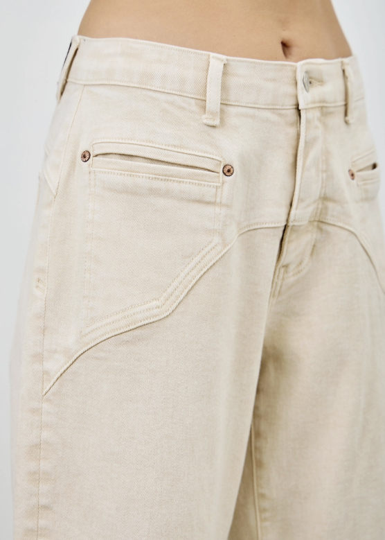 Close-up of a model wearing off-white denim jeans, showing the back pocket, button, belt loops, and waistband.