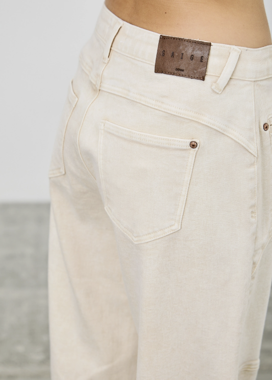 Close-up of a person wearing off-white denim jeans, showing the back pocket, waistband, and a brown leather brand patch that reads &