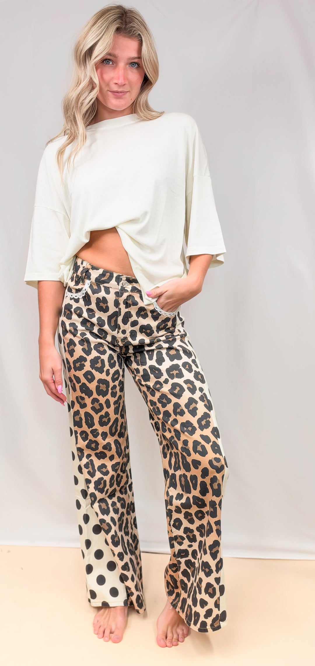 Woman wearing leopard and polka dot print pants with cream tee on plain background