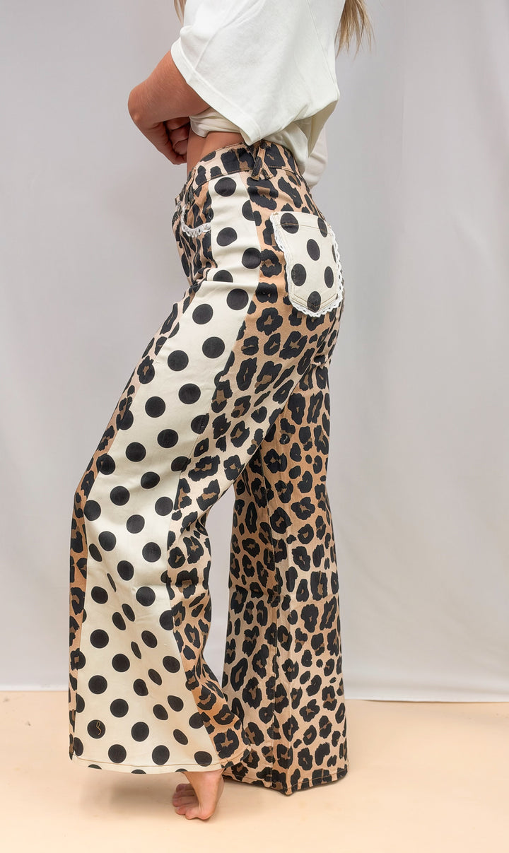 Woman shown from side view wearing leopard and polka dot print pants with cream tee on plain background