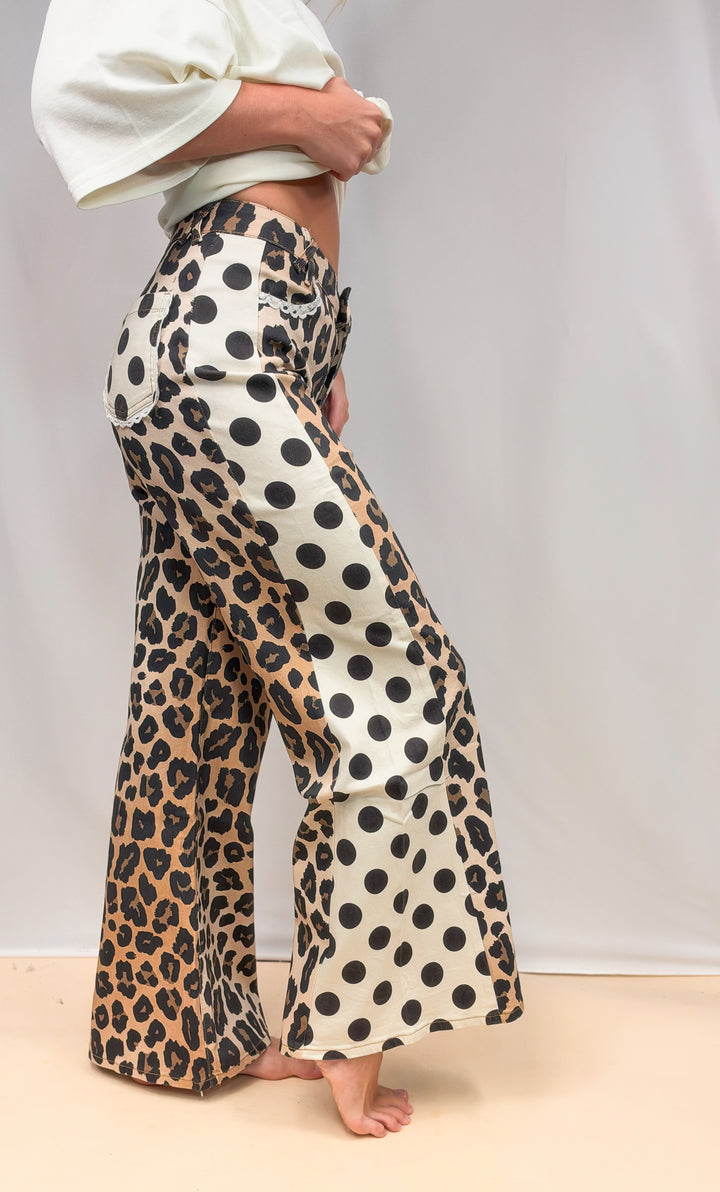 Woman shown from side view wearing leopard and polka dot print pants with cream shirt on plain background