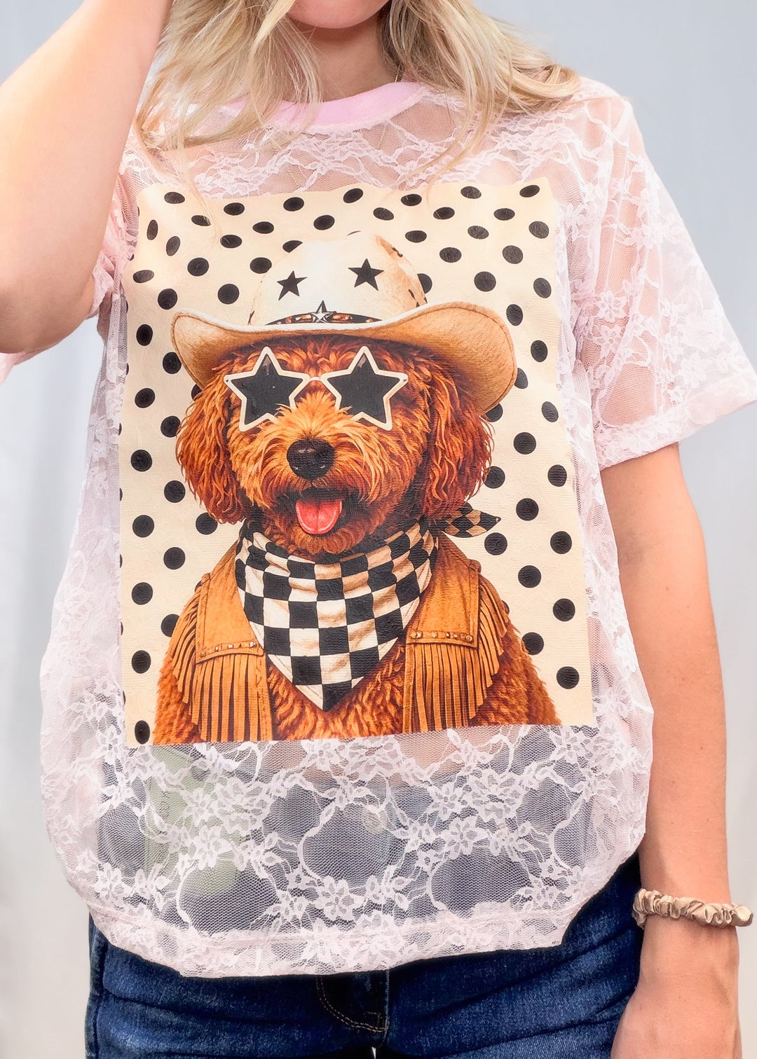 Woman wearing pink lace tee with poodle western graphic on front on plain background