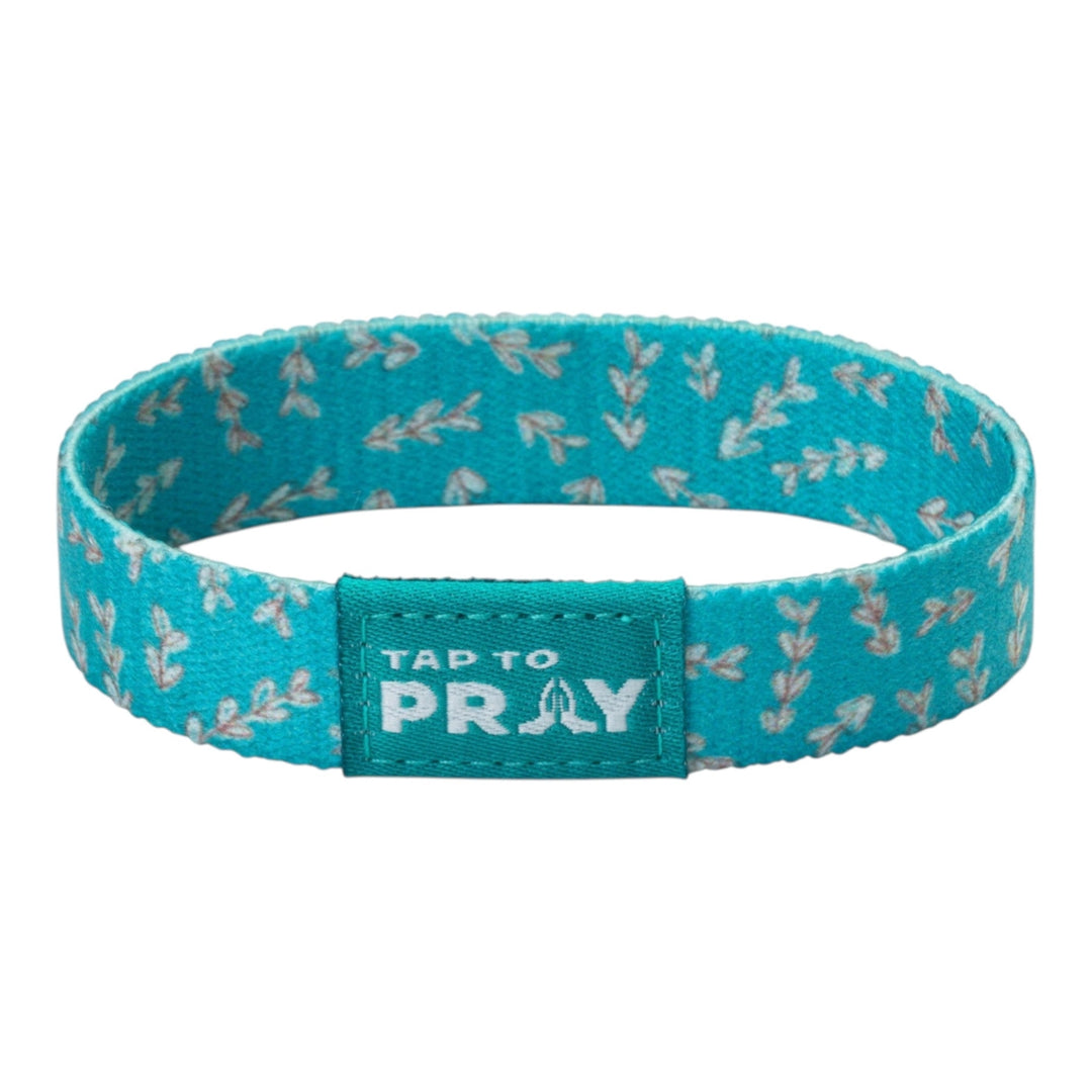 A teal fabric wristband with a repeating white leaf pattern and a central label that reads &