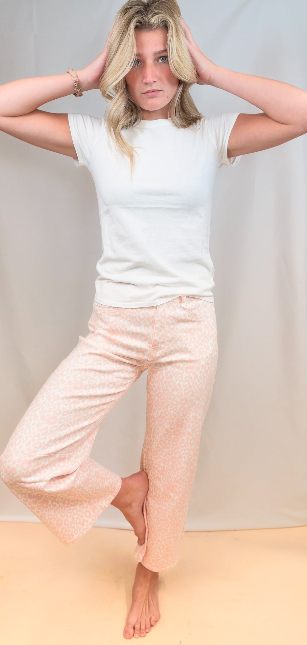 Woman wearing white tee with pink leopard pants on plain background