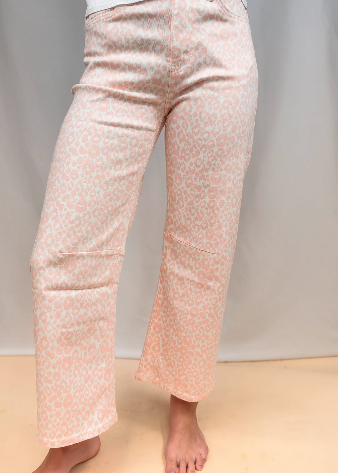 Woman shown from waist down wearing white tee and pink leopard pants on plain background