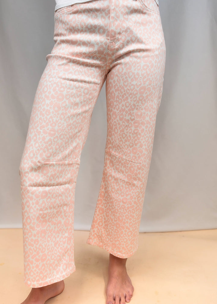 Woman shown from waist down wearing white tee and pink leopard pants on plain background