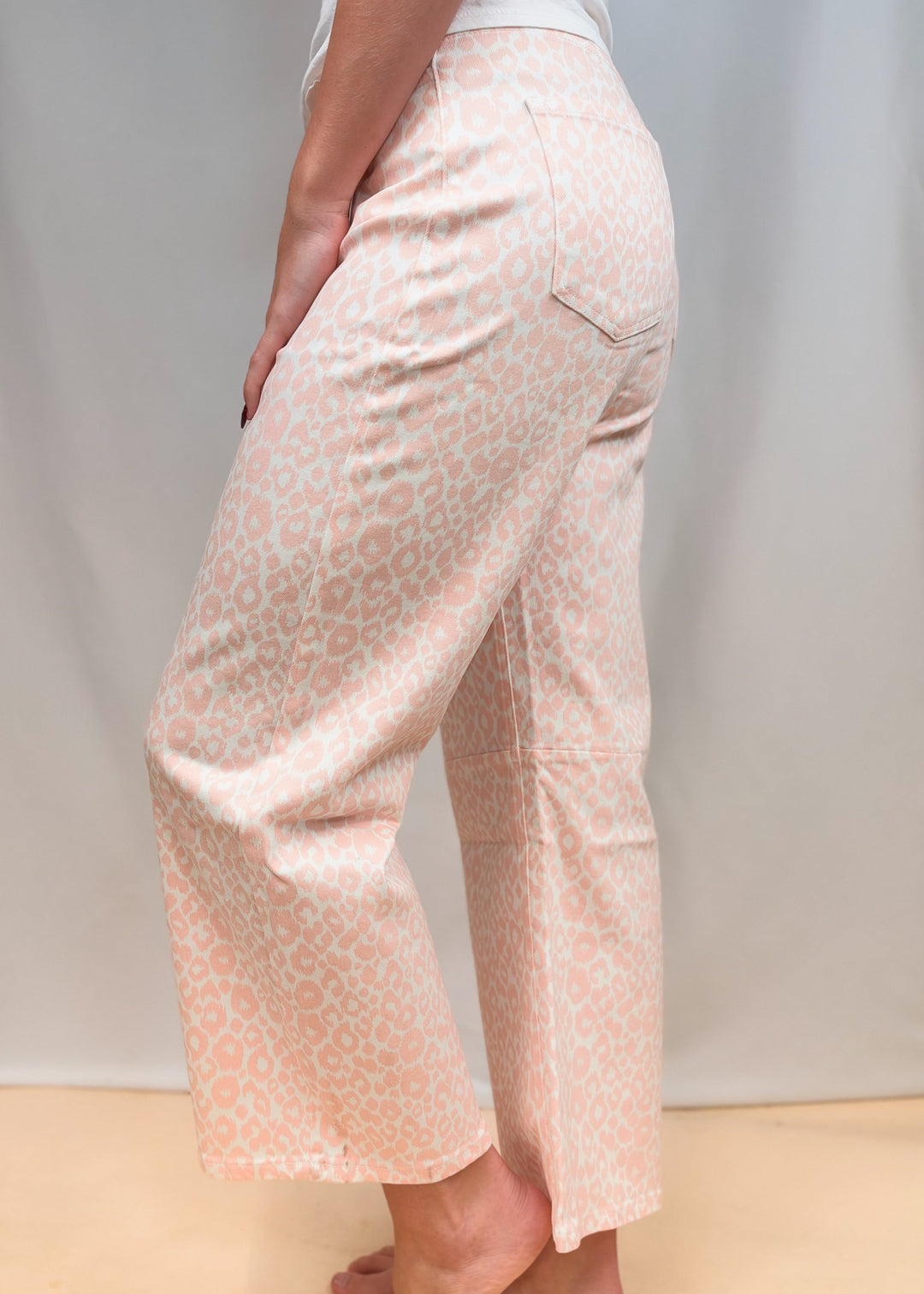 Woman shown from waist down wearing white tee and pink leopard pants on plain background