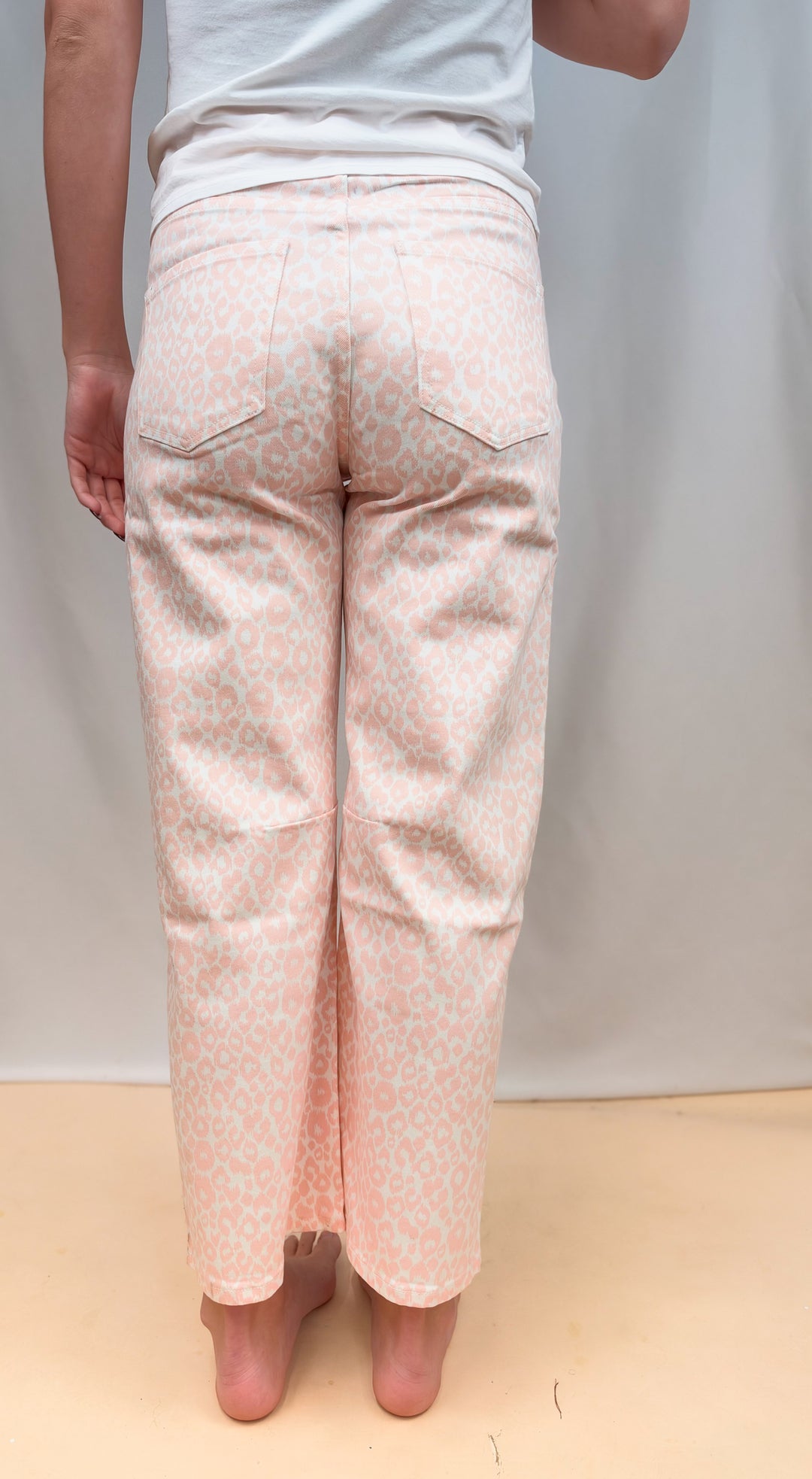 Woman shown from back view waist down wearing white tee and pink leopard pants on plain background