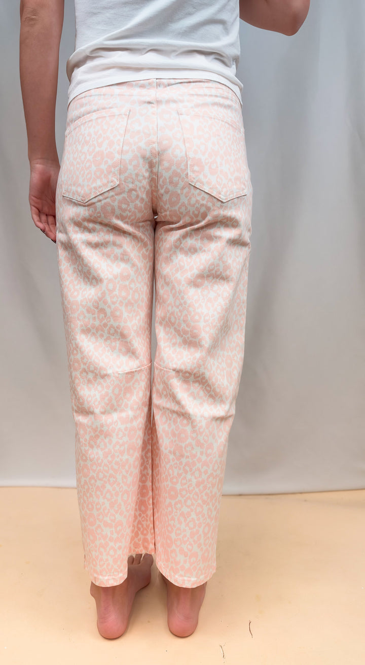 Woman shown from back view waist down wearing white tee and pink leopard pants on plain background