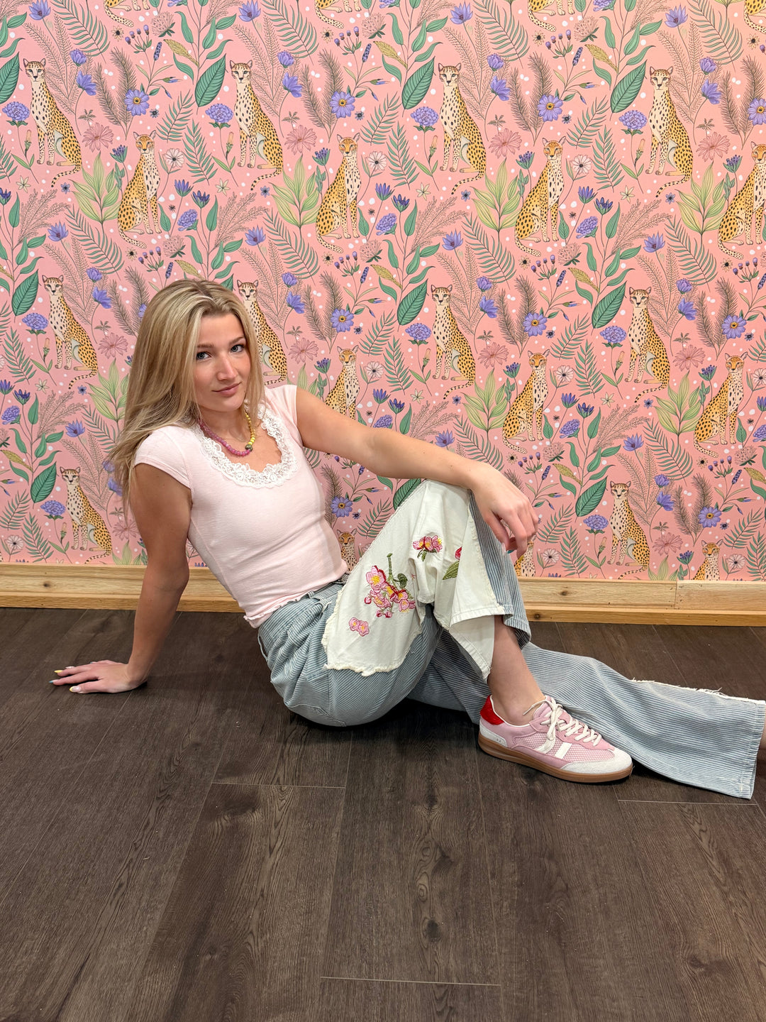 Woman sitting on a wooden floor with a pink floral wallpaper featuring leopards and flowers.