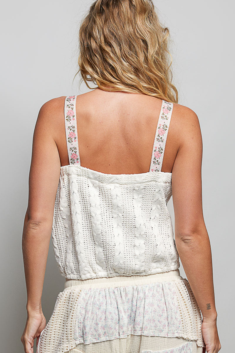Woman wearing a white lace top with floral straps on a plain background