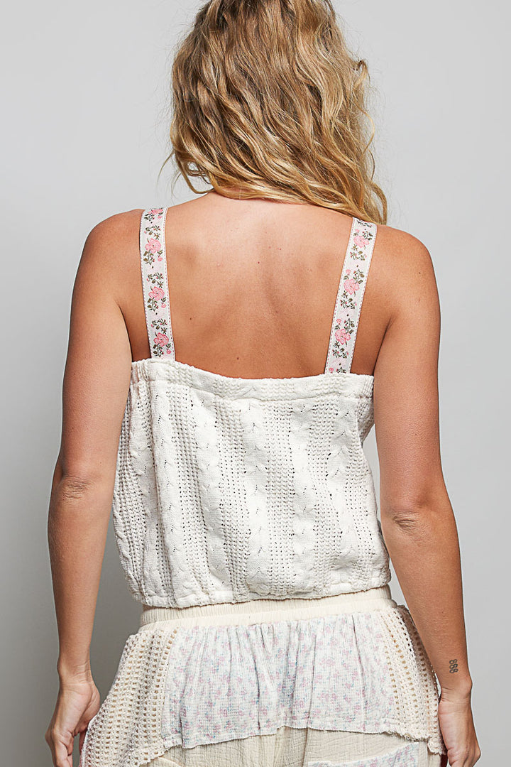 Woman wearing a white lace top with floral straps on a plain background