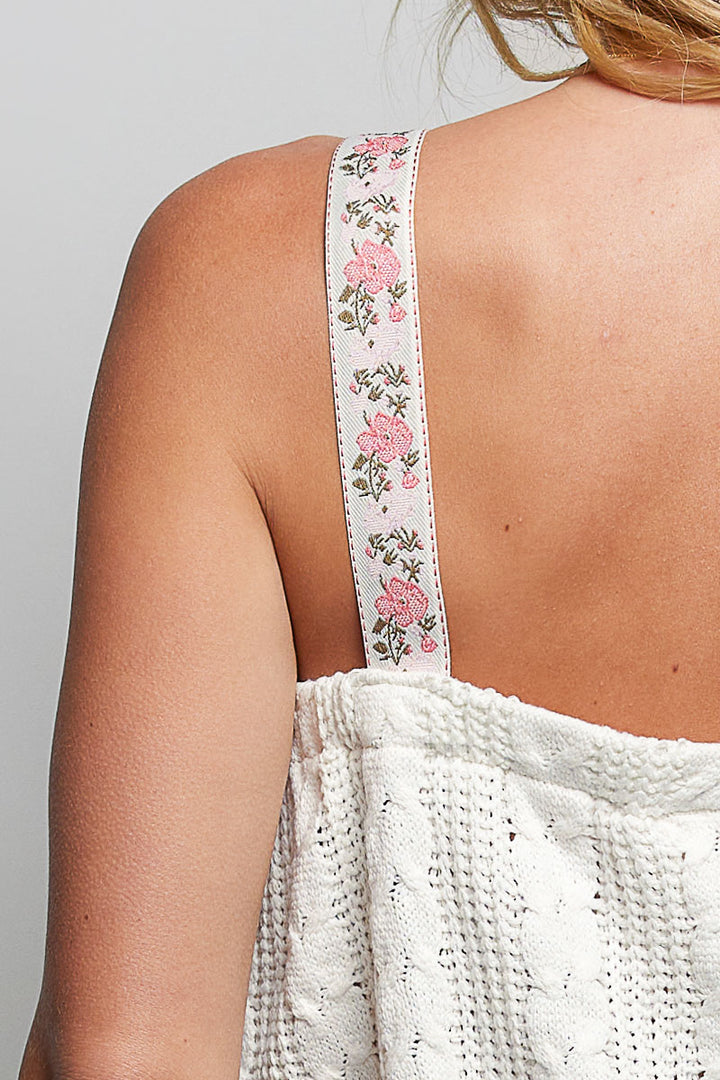 Close-up of a white crochet top with floral lace straps on a plain background