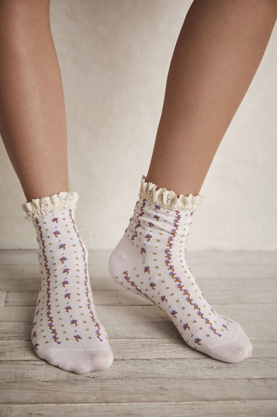 White socks with floral pattern worn by a person on a wooden floor.