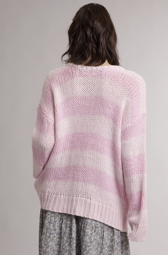 A person shown from the back wearing a chunky knit sweater with horizontal light pink and white stripes, paired with a gray patterned skirt, against a plain light gray background.