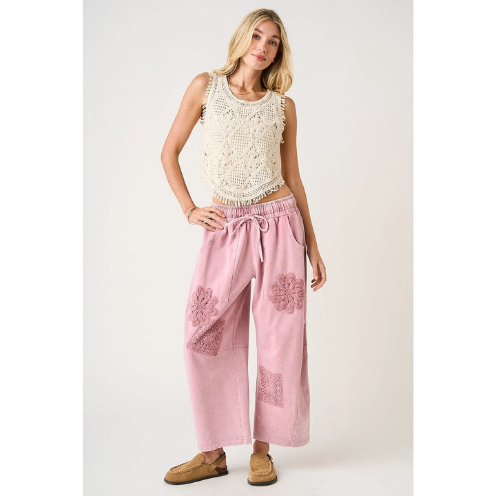 Woman wearing a white lace top and pink pants with floral embroidery on a white background